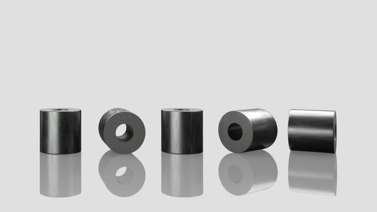 The image shows five cylindrical objects, with some having a hole through the center. These objects appear to be made of a dark, possibly metallic or composite material, and they are placed on a reflective surface. The cylinders vary slightly in orientation, with some standing upright and others lying on their sides. The reflective surface creates a mirrored effect, showing the bottom part of the cylinders.