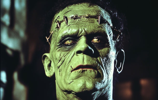 This image depicts a character with a greenish complexion and a prominent forehead, which is characteristic of Frankenstein's monster from classic horror films. The lighting and makeup style suggest it is from an older movie, possibly the 1931 film "Frankenstein" directed by James Whale, where Boris Karloff famously portrayed the monster.