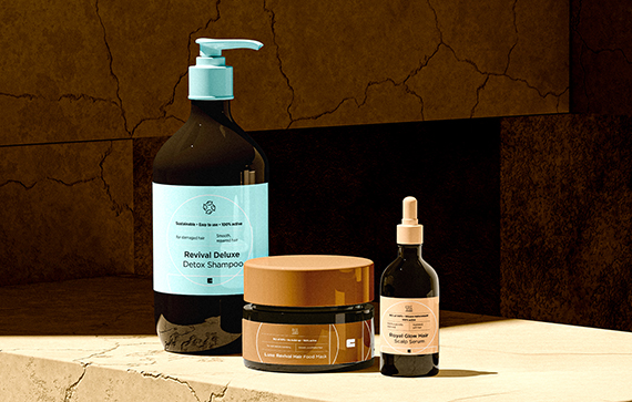 The image shows three hair care products placed on a stone surface with a cracked wall in the background. The products are:

1. A large bottle with a pump dispenser labeled "Revival Deluxe Detox Shampoo."
2. A jar labeled "Lush Herbal Hair Food Mask."
3. A dropper bottle labeled "Royal Glow Hair Scalp Serum."

These products appear to be part of a hair care routine aimed at detoxifying, nourishing, and promoting scalp health.