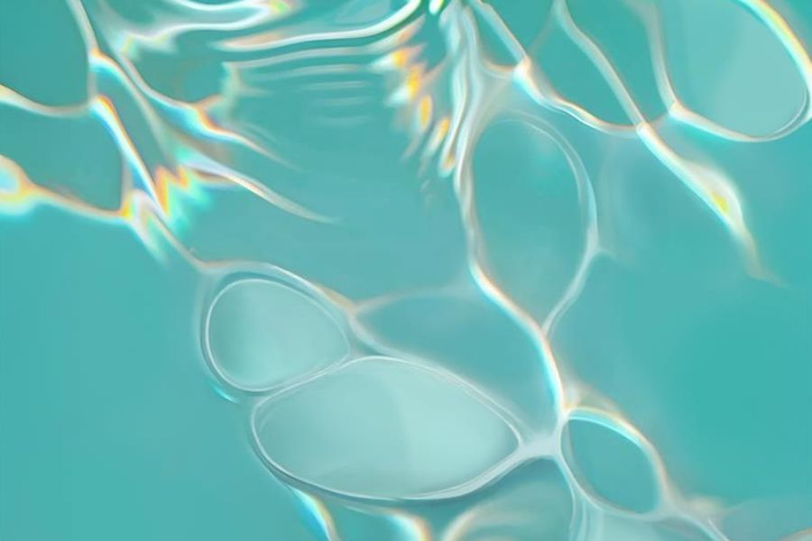 This image shows the surface of water with light reflecting and refracting through it, creating a pattern of bright, wavy lines and shapes. The water appears clear and has a blue-green tint, suggesting it might be in a pool or a similar setting. The light patterns are caused by the interaction of sunlight with the moving water surface.