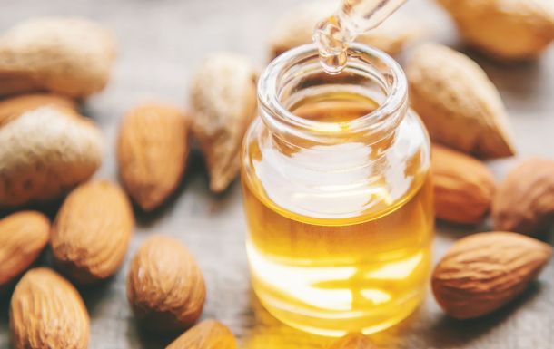 A small glass bottle of almond oil with a dropper, surrounded by whole almonds.