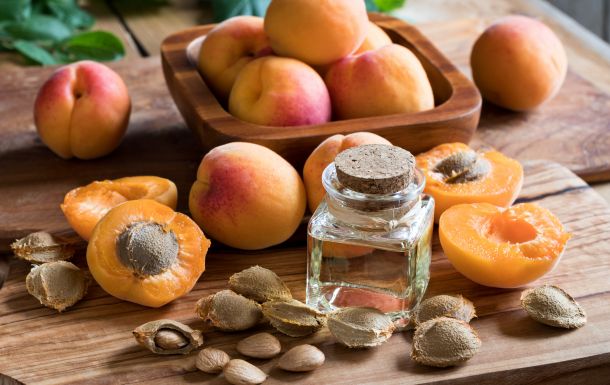 The image shows a collection of apricots, both whole and halved, along with apricot pits and a small bottle of oil. The apricots are displayed on a wooden surface, and the bottle of oil is likely apricot kernel oil, which is derived from the seeds of apricots. Apricot kernel oil is often used in cooking, cosmetics, and skincare products due to its moisturizing properties. The image highlights the natural and fresh appearance of the apricots and the oil.