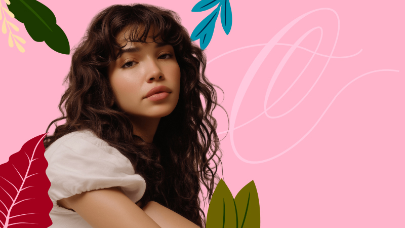 Portrait of a young woman with curly hair on a pink background with decorative leaves
