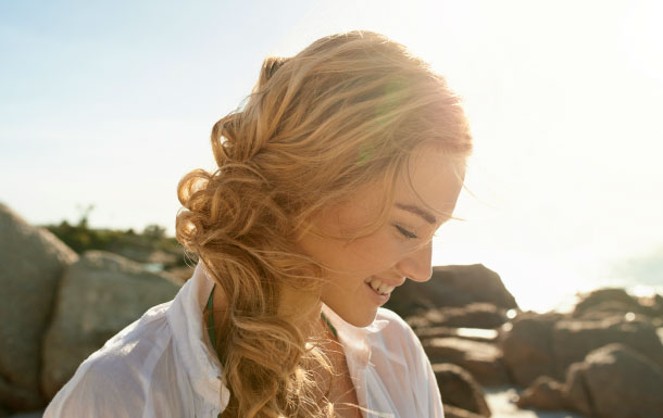 Woman with long blonde hair outdoors by the water in bright sunlight